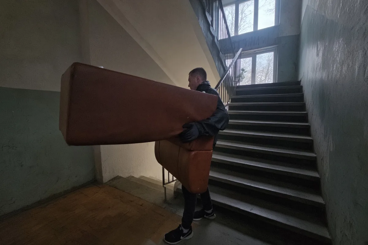 Грузчик несёт коричневый матрас по лестнице подъезда