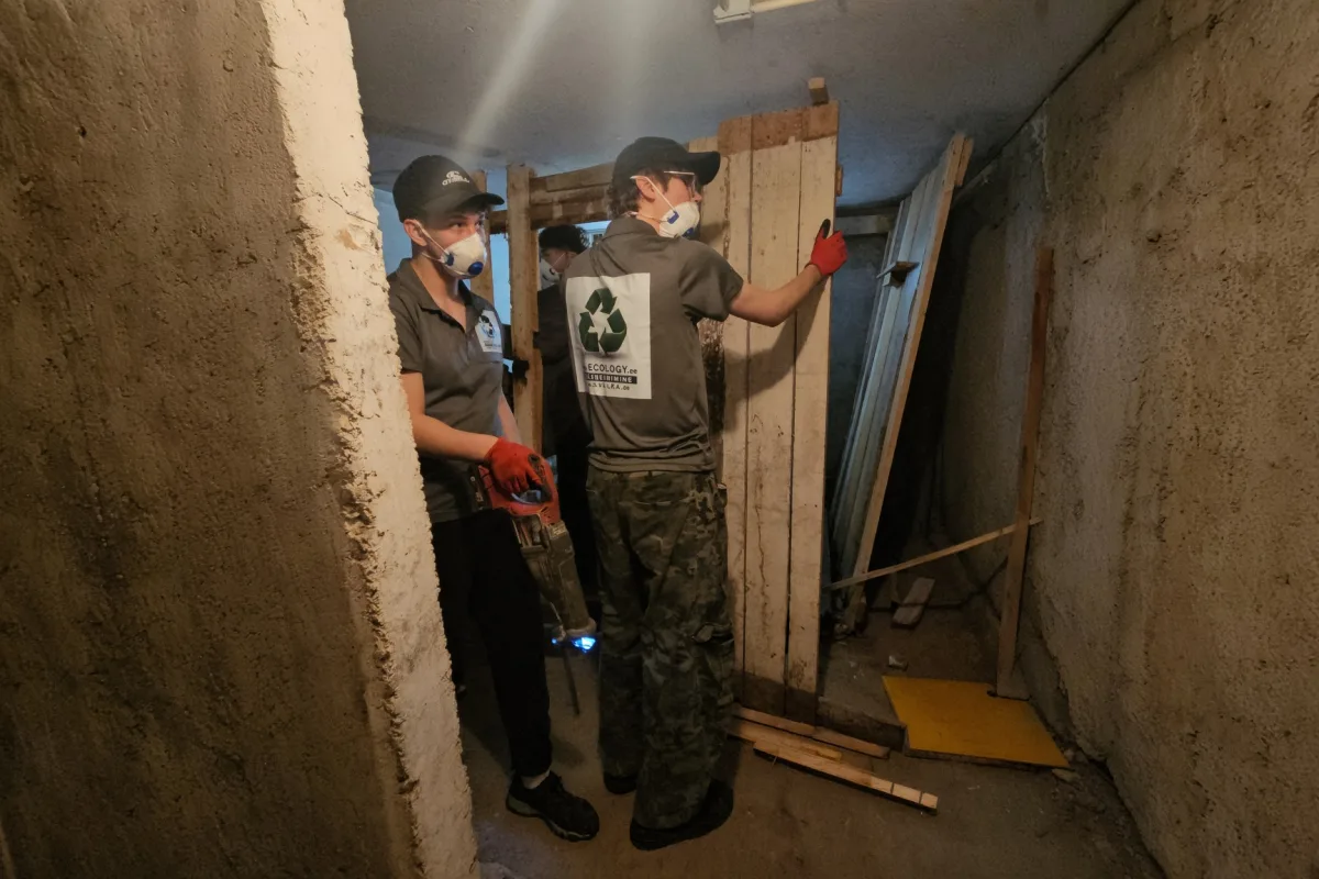 Грузчики в масках разбирают деревянную кладовку в подвале