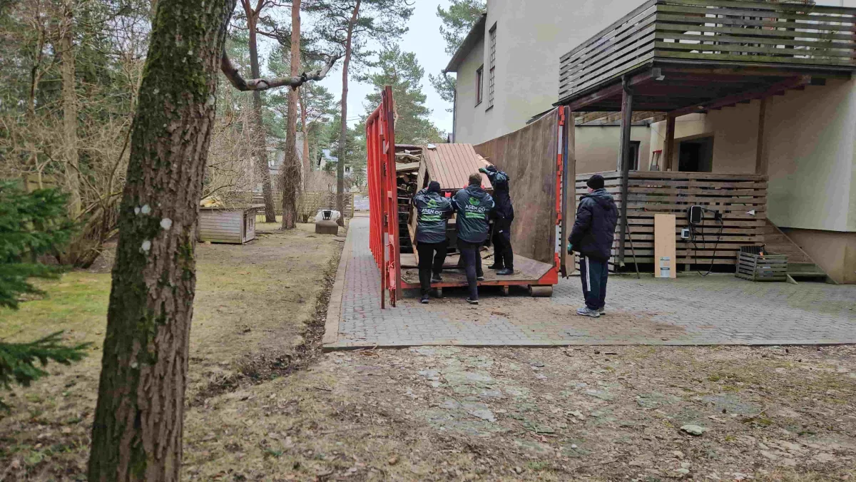 Грузчики заносят вещи в красный контейнер у частного дома