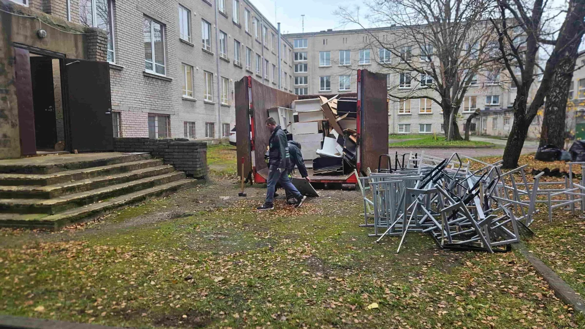 Грузчики несут вещи к контейнеру мимо металлических стульев