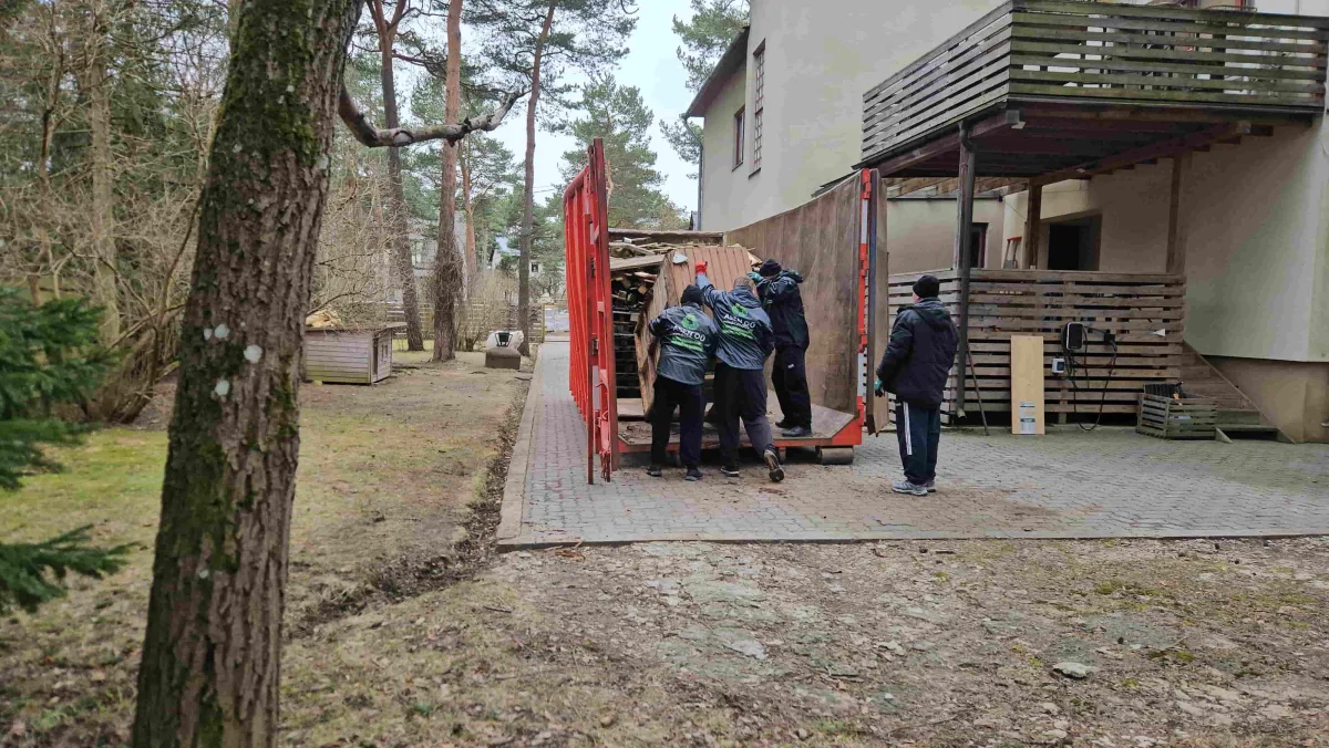 Рабочие в спецовках у красного контейнера рядом с домом