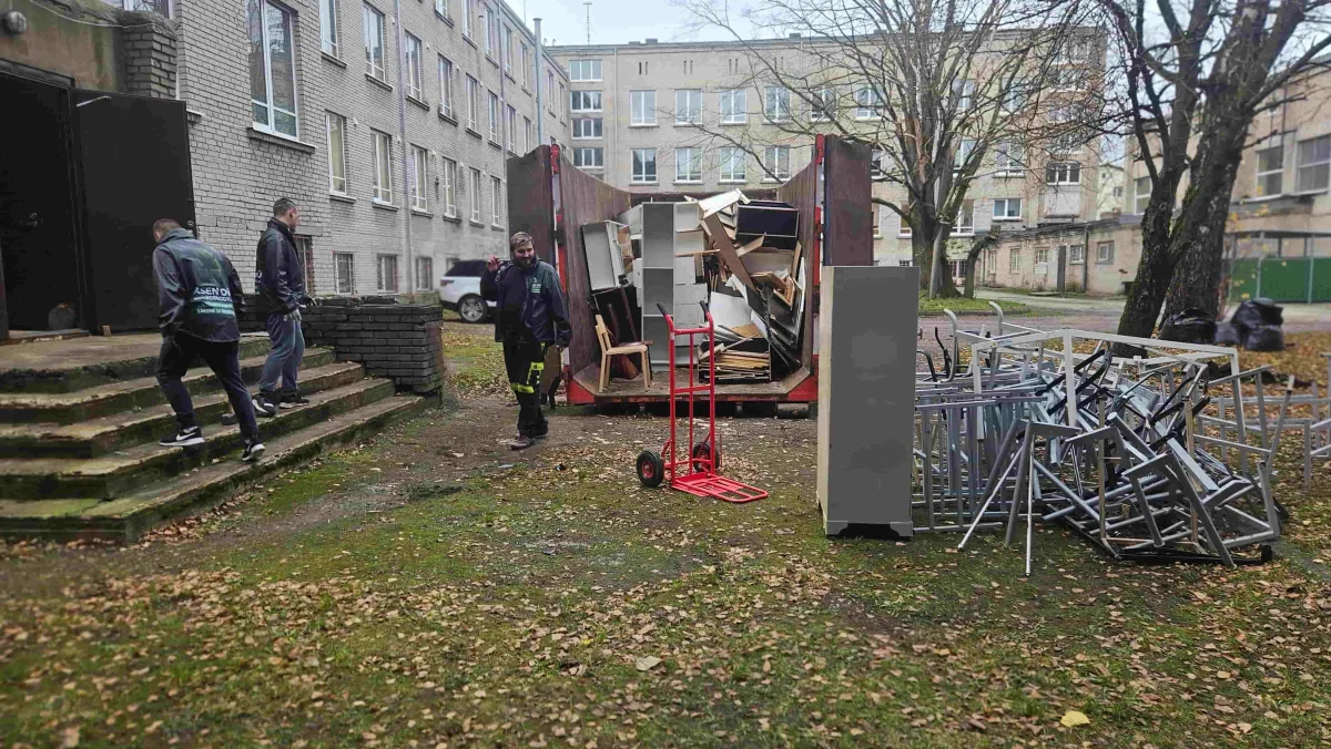 Грузчики выносят хлам и старые стулья к контейнеру во дворе