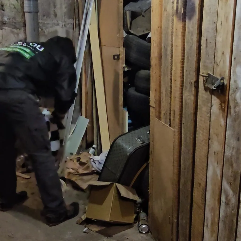 Грузчик разбирает хлам в деревянной кладовой подвала