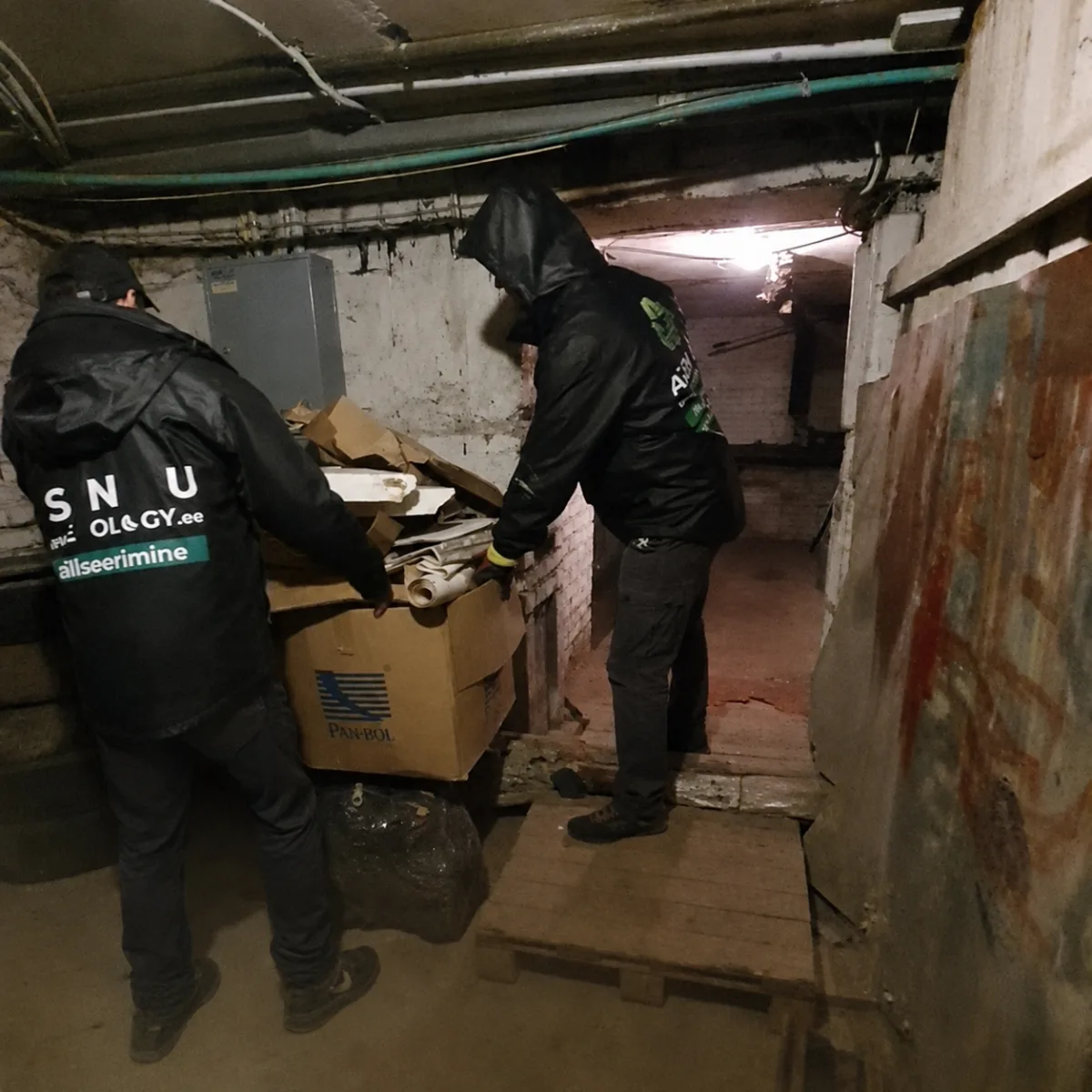 Двое грузчиков разбирают коробки в узком подвальном проходе