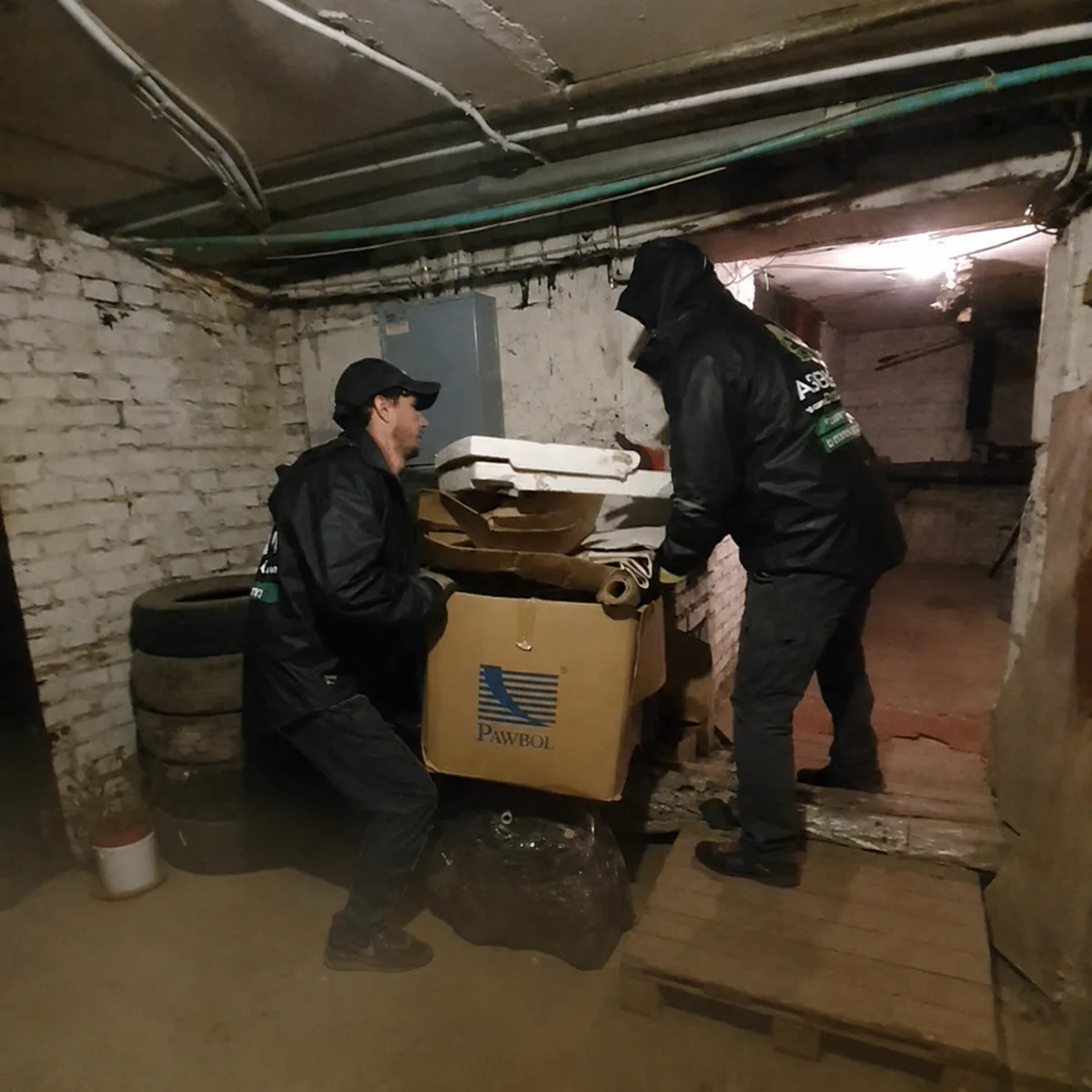 Грузчики выносят коробки и хлам из кирпичного подвала
