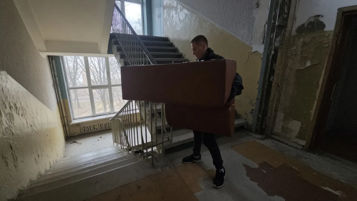 Грузчик несёт диван по лестнице подъезда