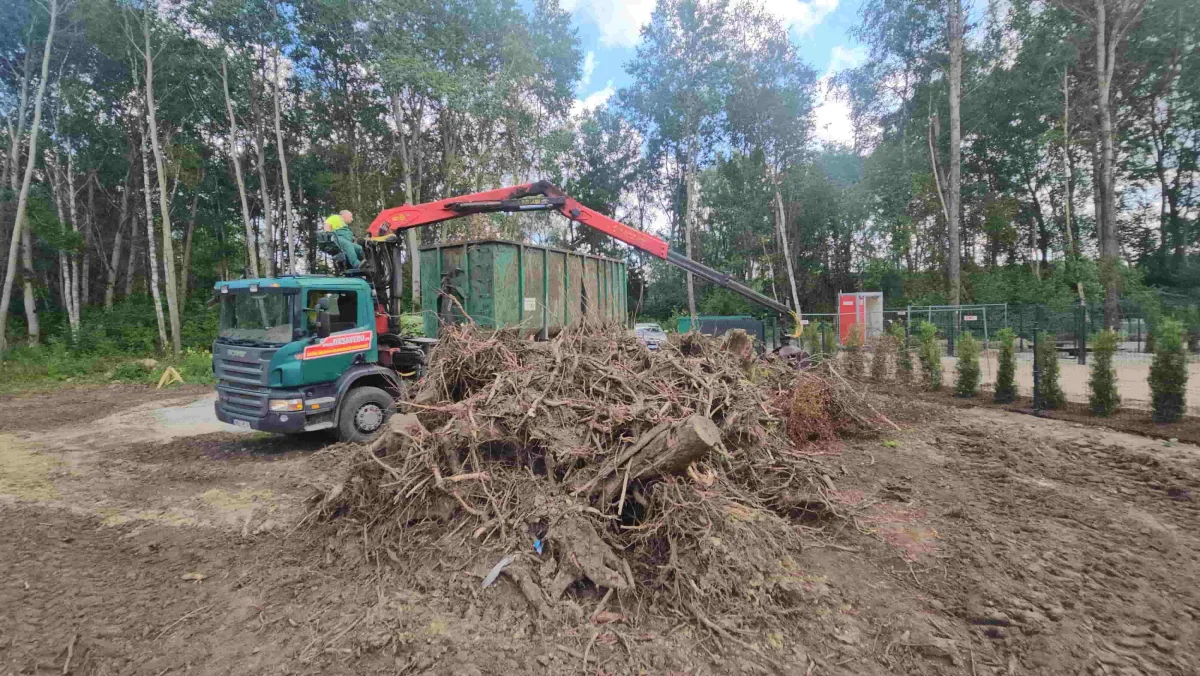 Грузовик с грейфером у кучи веток и стволов на участке