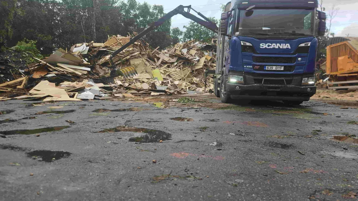 Синий Scania с краном у кучи древесных отходов