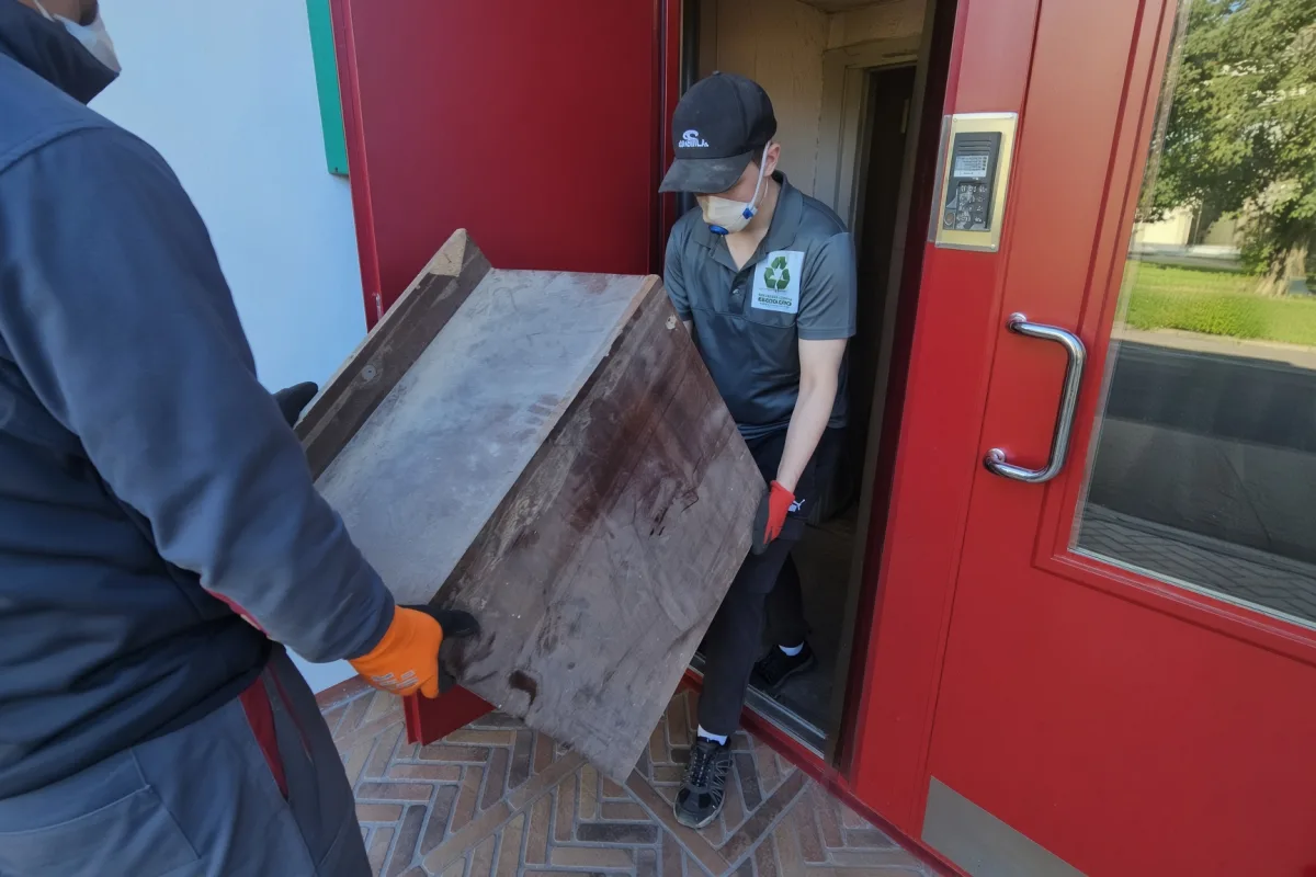 Грузчики в перчатках выносят тяжёлый ящик из красной двери