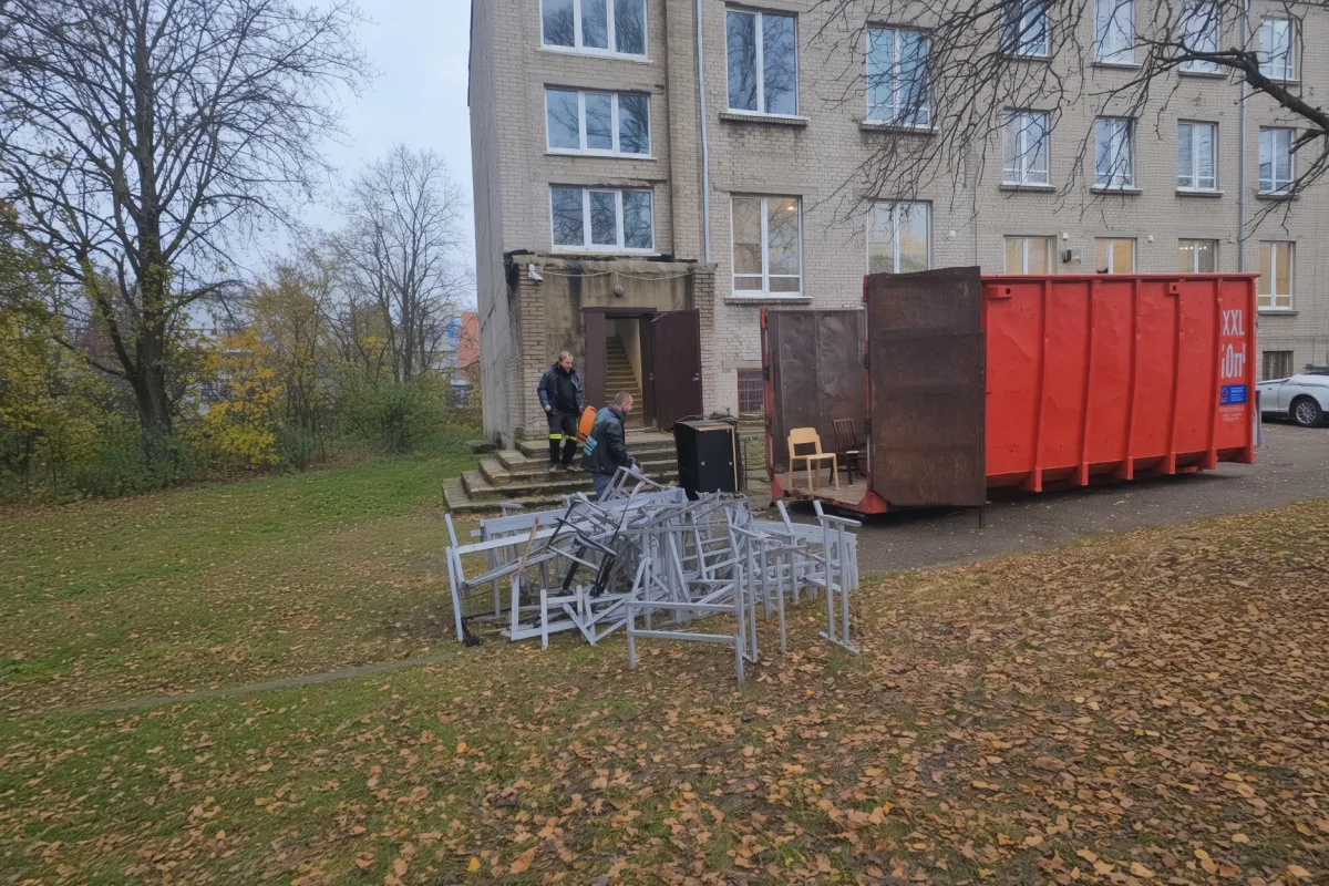 Металлические рамы на газоне у здания и красный контейнер