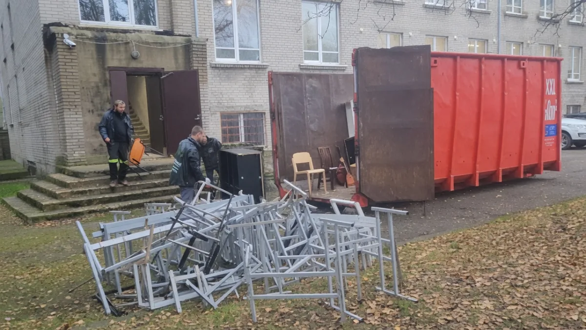 Грузчик у груды металлических стульев перед контейнером