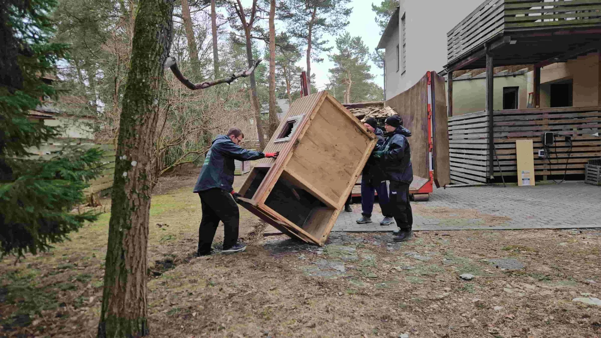 Двое рабочих выносят старый деревянный шкаф во двор