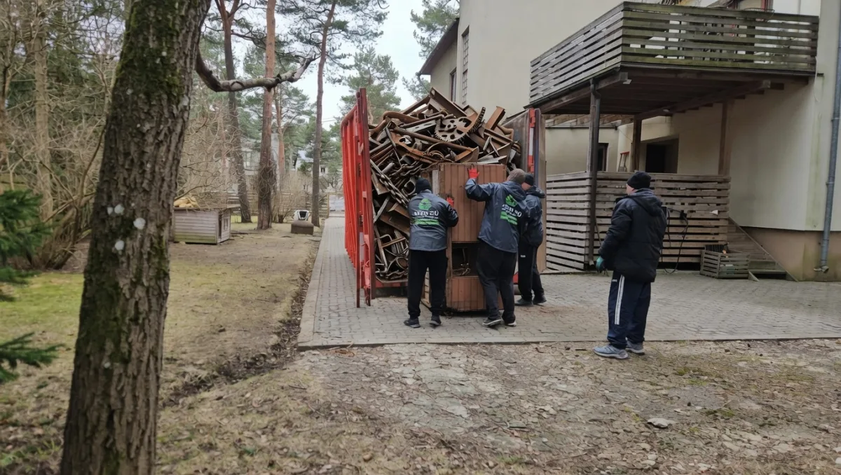 Грузчики складывают старые доски в красный контейнер у дома